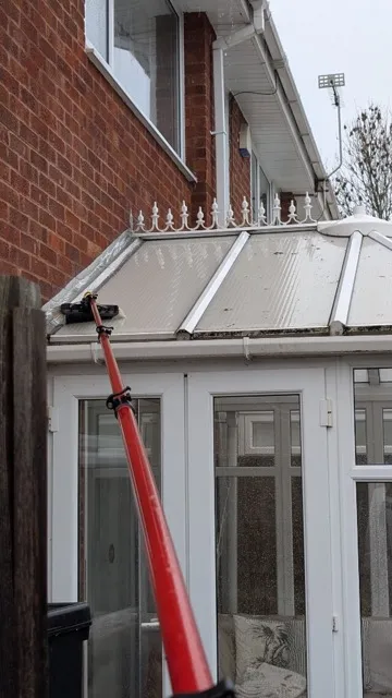 Telescopic brush cleaning a white uPVC conservatory roof
