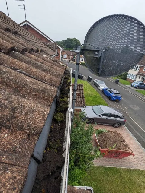Blocked gutter filled with moss and debris before clearing